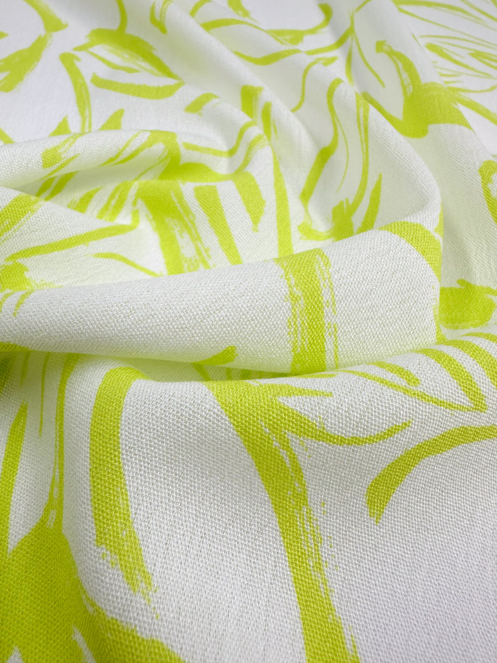 A close-up image of Super Cheap Fabrics' Soft Cotton - Love Bird - 140cm fabric showcases a vivid lime green abstract pattern. The 100% cotton material appears to have a slightly textured surface, featuring sweeping, brushstroke-like lines and shapes that make it an ideal fabric for summer.