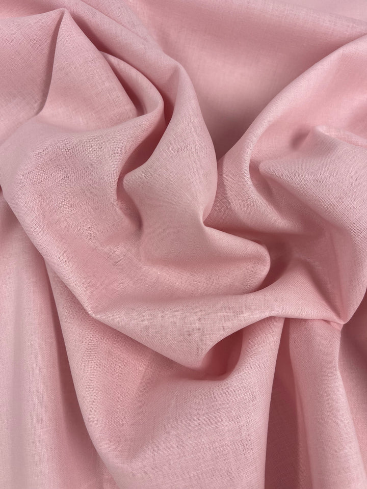 A close-up view of the soft, crumpled Pure Linen - Pearl - 140cm fabric from Super Cheap Fabrics. The texture of this light pink linen appears smooth and slightly translucent, with natural folds and creases creating a subtle play of light and shadows.