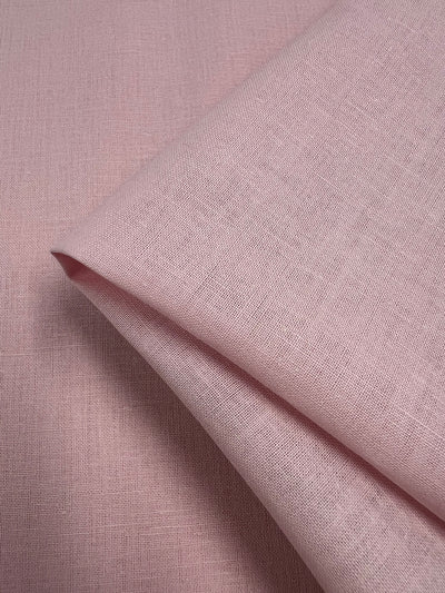 A close-up image of Pure Linen - Pearl - 140cm by Super Cheap Fabrics, folded neatly. The texture of the lightweight fabric and the natural weave pattern are clearly visible, displaying a soft, slightly rough surface.