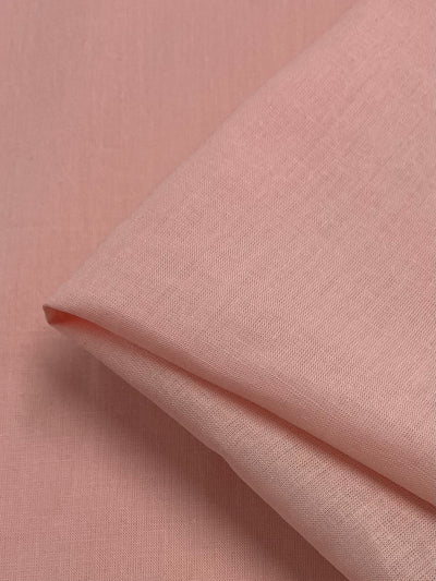 A close-up view of Super Cheap Fabrics' Pure Linen in Salmon Pink reveals its 100% linen composition. The 140cm wide material has a smooth yet slightly textured appearance, highlighting its fine weaving details. The edges are neatly aligned, creating a clean and polished look.