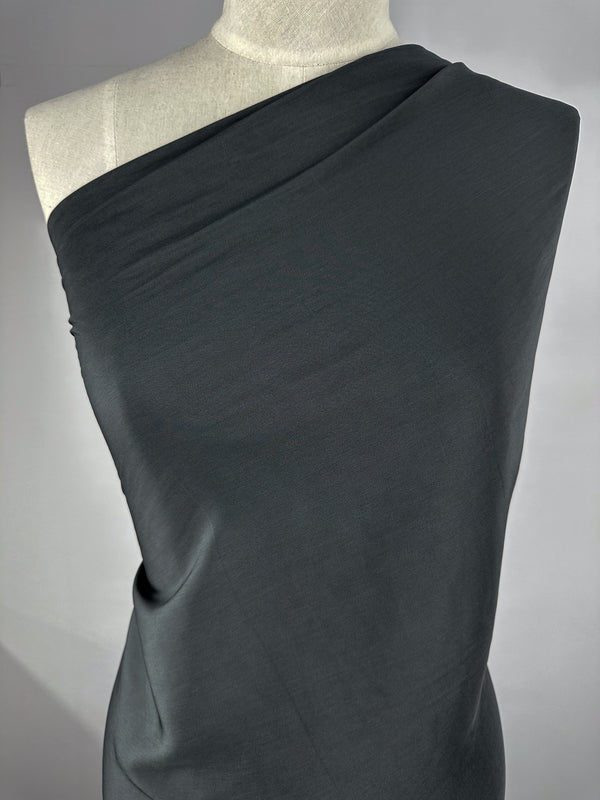 A dress form draped with charcoal microfibre fabric from Super Cheap Fabrics, styled in an asymmetrical one-shoulder design. The smooth, opaque material is wrapped neatly around the upper part of the dress form, showcasing elegant lines and sophisticated craftsmanship.