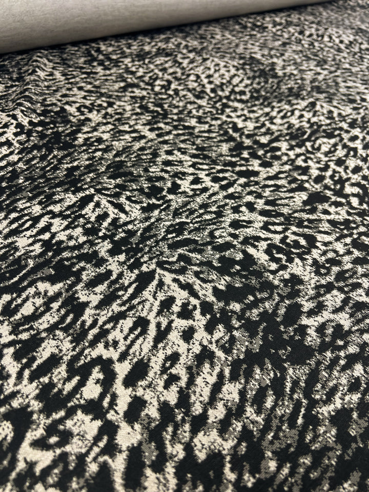 Close-up of **Super Cheap Fabrics' Textured Knit - Leopard**, a medium-weight fabric featuring a black and white abstract pattern resembling scattered, irregularly shaped spots. The knit texture appears rough, and the design creates a dynamic, almost chaotic visual effect with generous stretch across its 145cm width.