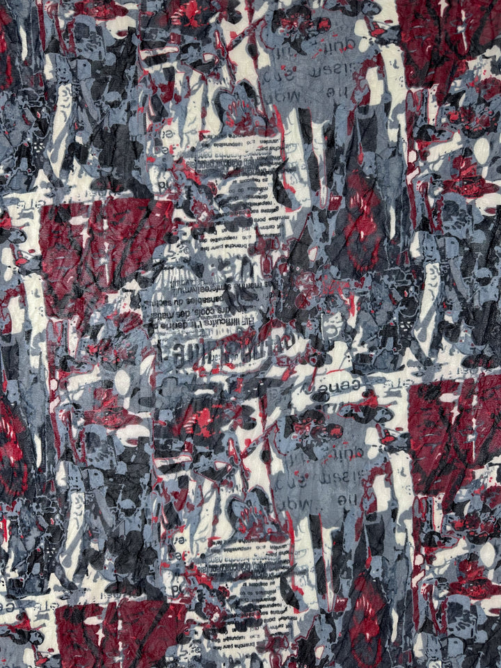 The Printed Mesh - Read - 120cm from Super Cheap Fabrics showcases an abstract design featuring a chaotic collage of red, grey, black, and white textures. This lightweight fabric includes torn and overlapping printed text fragments, resulting in a visually complex pattern that combines organic and geometric shapes.