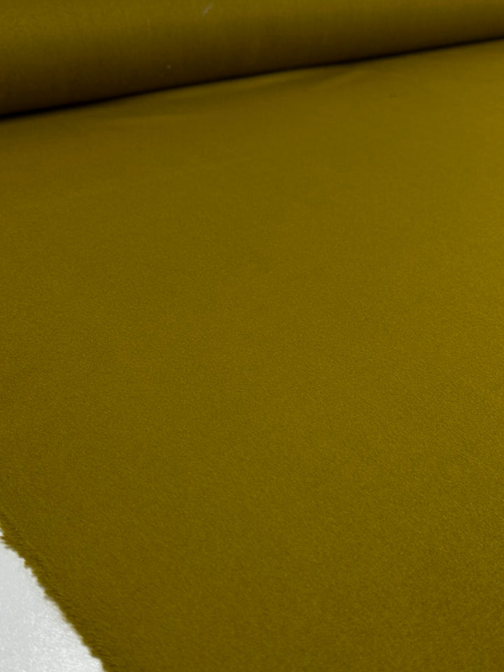 A close-up of Super Cheap Fabrics' Wool Cashmere in Amber Green (150cm wide), partially unrolled to showcase its smooth, even texture and luxurious softness across most of the surface.