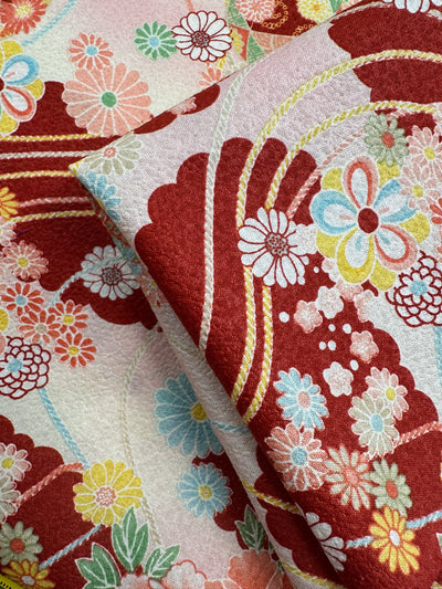 Close-up of Super Cheap Fabrics’ Japanese Printed Cotton - Textured Crane Garden (112cm), featuring vibrant red, pink, and yellow floral patterns with intricate Japanese motifs and overlapping detailed flowers and curved lines.