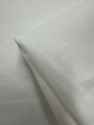 A close-up of Super Cheap Fabrics’ Pure Linen - Off White 01 (150cm) shows its breathable texture and smooth, linen-like surface, neatly folded at one corner against a matching background.