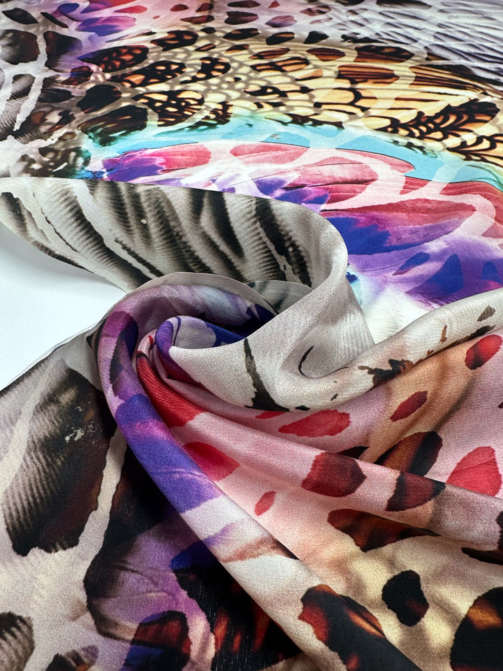 A close-up of Super Cheap Fabrics' Pure Silk - Electric Bloom (140cm), showcasing vibrant abstract prints in brown, purple, pink, and yellow, swirled on a white surface—ideal for high-end fashion.