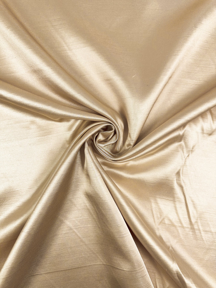 Super Cheap Fabrics' Shantung Satin in Gold (150cm) features a lustrous, light gold finish with smooth, gathered folds and a soft, reflective texture.