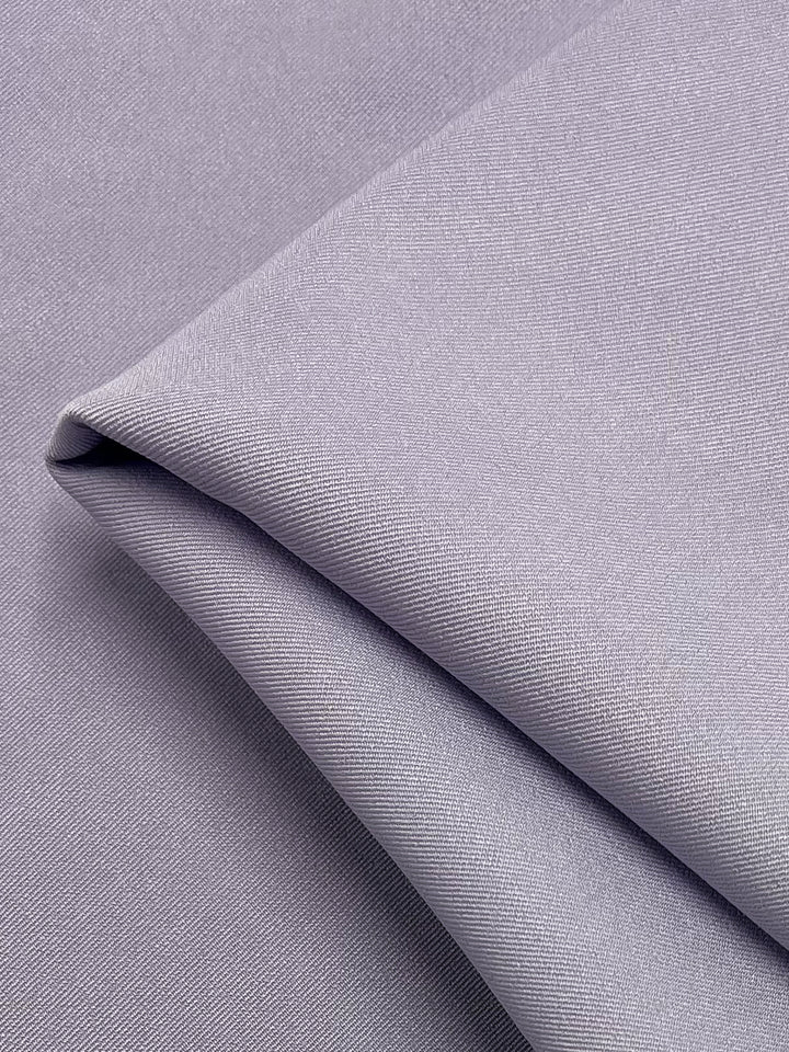 A close-up photograph of the Twill Suiting in Lavender Blue from Super Cheap Fabrics, showcasing its smooth and slightly textured surface. The fabric appears soft and lightweight, with subtle, fine diagonal weave patterns typical of versatile woven material.