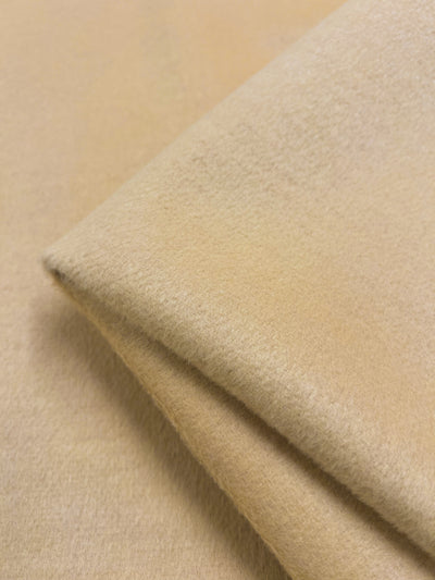 A close-up image of Super Cheap Fabrics' Wool Cashmere - Autumn Blonde - 150cm, a beige folded piece of fabric with a soft and fuzzy texture. The heavy weight fabric appears thick and warm, likely made from a wool cashmere blend or similar material.