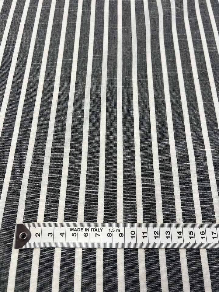 A close-up view of the Linen Cotton fabric from Super Cheap Fabrics, featuring dark grey stripes alternating between narrow and wide patterns. The fabric, made from durable natural fibers, has a measuring tape laid across it indicating distances in centimeters and labeled "MADE IN ITALY". This particular roll is 145cm wide.