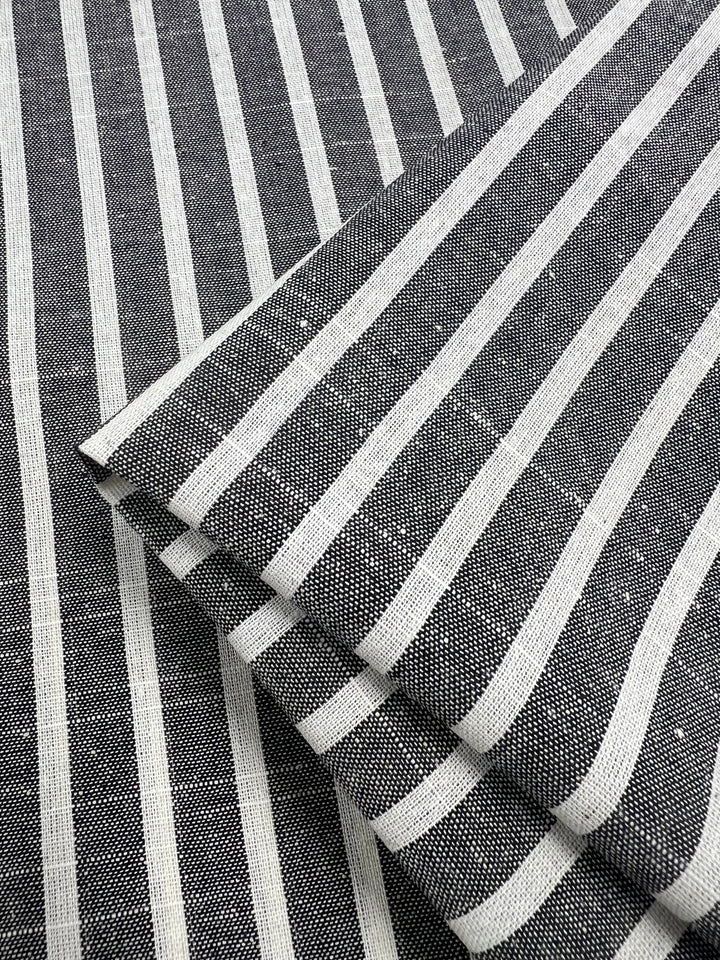 Close-up image of a folded Linen Cotton - Dark Grey Stripe fabric from Super Cheap Fabrics. The pattern features evenly spaced vertical white stripes on a dark grey background, creating a classic, textured look. This natural fiber fabric appears to be neatly arranged, highlighting its durable design clearly.