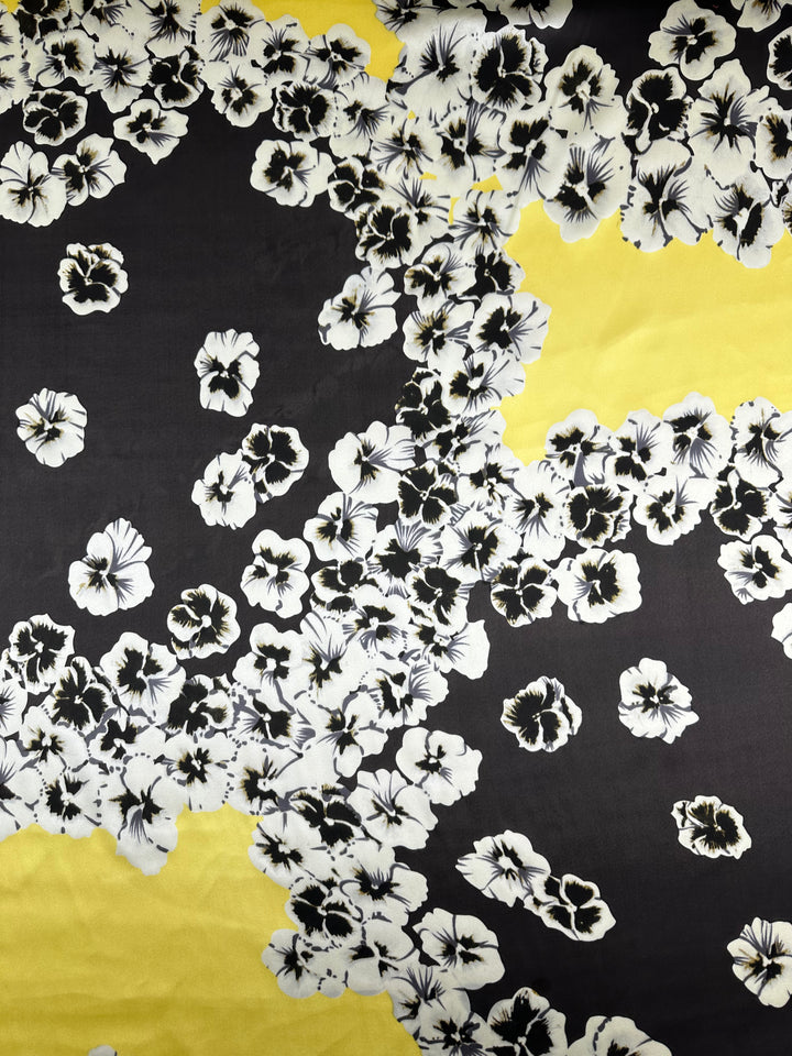 The Printed Stretch Silk - Ramona from Super Cheap Fabrics is adorned with a floral design featuring clusters of white flowers with black centers scattered across a yellow and dark grey background. This fabric's dense and sparse pattern distribution creates a visually striking contrast, making it ideal for high-end fashion attire.