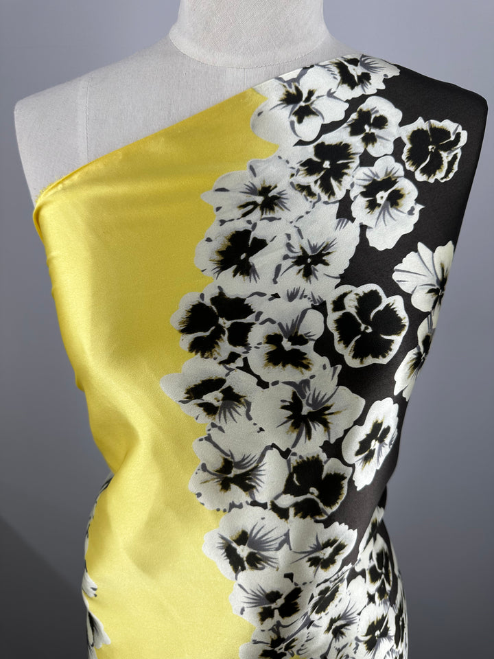 A mannequin showcasing the Printed Stretch Silk - Ramona - 100cm from Super Cheap Fabrics, featuring a striking bold design. One half of the fabric is yellow, and the other half is black, both adorned with densely packed white and black floral patterns. This dazzling contrast between dark and bright hues makes it perfect for high-end fashion attire.