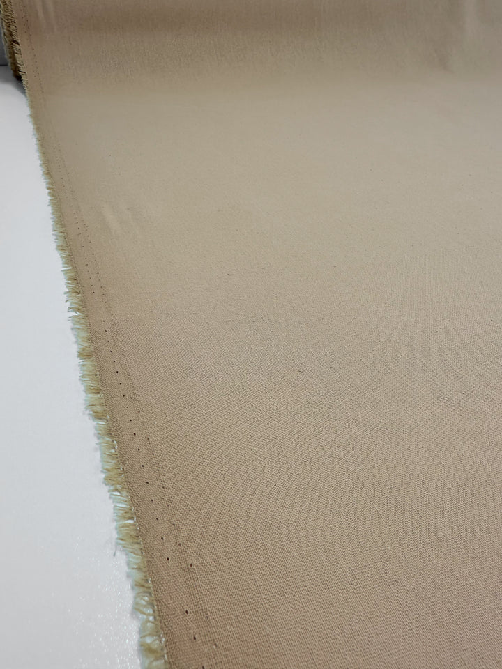 The Super Cheap Fabrics Ramie Linen - Hazelnut (150cm) is spread out, revealing its smooth texture and slightly frayed edges on one side, laid on a flat white surface.