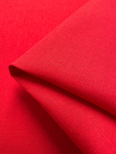 A close-up of the **Ramie Linen - True Red - 150cm** from **Super Cheap Fabrics**, showcasing the neatly folded bright red fabric. The intricate weave pattern of the natural fibers is visible, offering a vibrant and textured appearance.