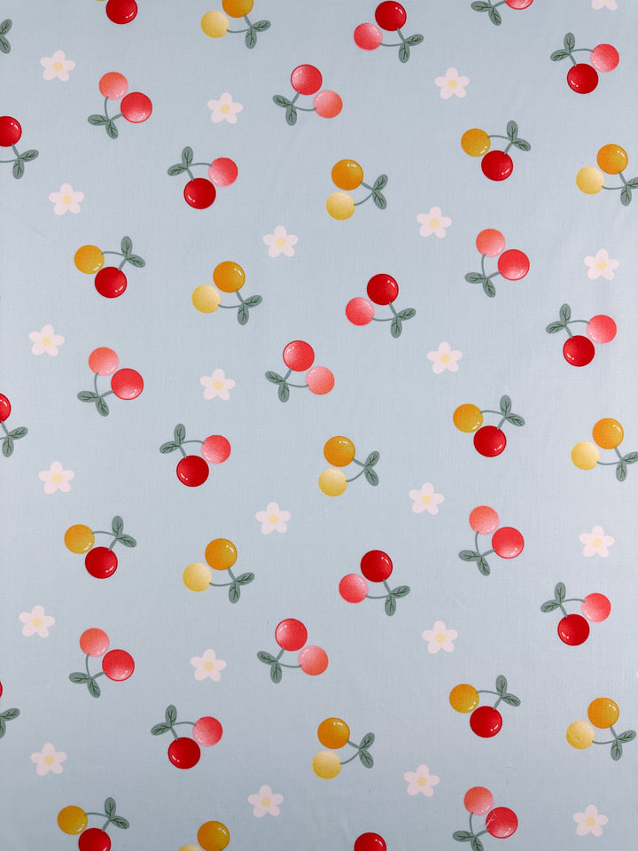 The Printed Cotton - Ripe - 150cm by Super Cheap Fabrics showcases a pale blue background with clusters of red and yellow circles that resemble fruit, complemented by small white flower motifs. Made from natural cotton fibers, this fabric offers both vibrancy and comfort to any setting.