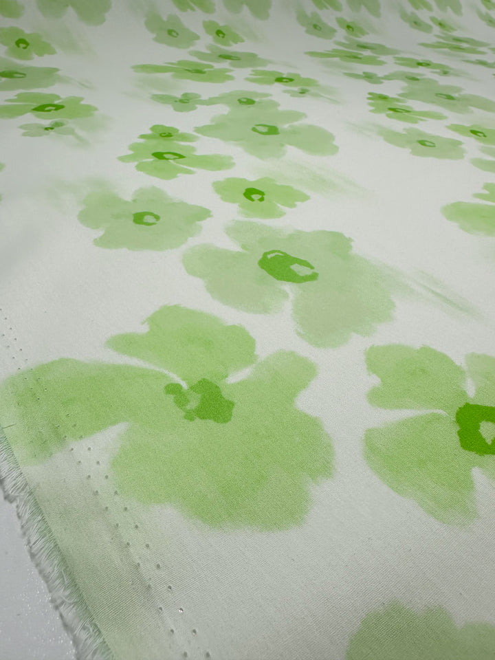 Discover the Printed Cotton - Lime Bloom from Super Cheap Fabrics, featuring a delicate light green floral pattern against a soft pale background. This fabric boasts abstract flowers scattered across its surface, crafted from natural cotton fibers for a slightly textured edge. It's perfect for creating both clothing and household items. With a width of 150cm, it meets your versatile sewing needs seamlessly.