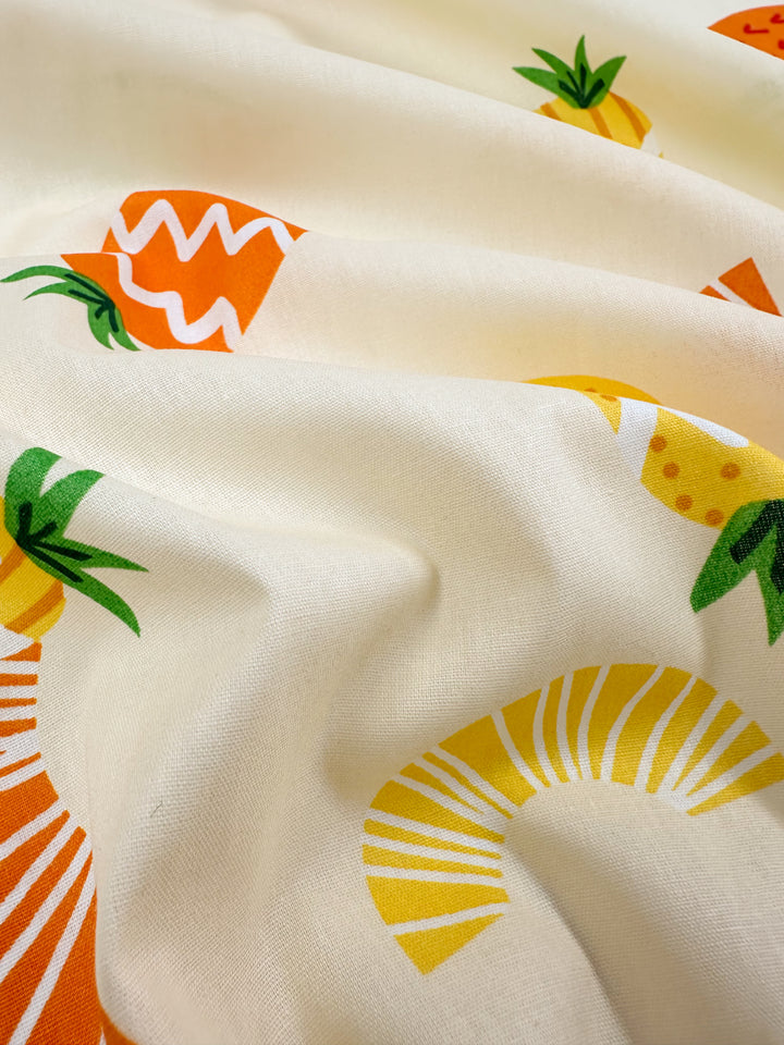 The Printed Cotton - Summer - 150cm by Super Cheap Fabrics is a lightweight fabric adorned with a cheerful fruit pattern showcasing oranges, pineapples, and bananas in vivid shades of orange, yellow, and green, made from natural cotton fibers and elegantly flowing in soft folds.