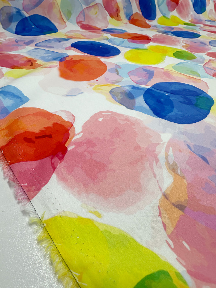 Super Cheap Fabrics presents "Printed Cotton - Bubble - 150cm," featuring vibrant watercolor-style circles in pink, red, blue, yellow, and green. Made from natural cotton fibers, it's ideal for crafting both clothing and household items. The edge of the fabric is visible on the left side.