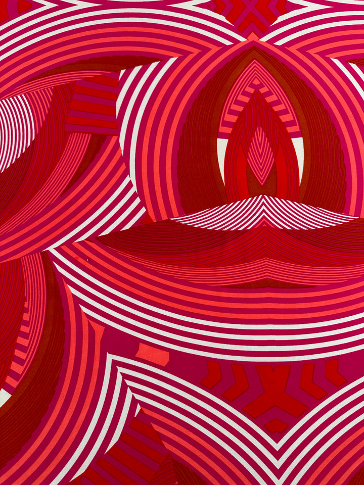 A vibrant abstract artwork featuring intricate patterns of concentric curves and lines on Printed Lycra - Wonka - 150cm by Super Cheap Fabrics. Dominated by red, pink, and white hues, the design creates a sense of dynamic movement and depth with its repetitive geometric shapes and flowing contours.