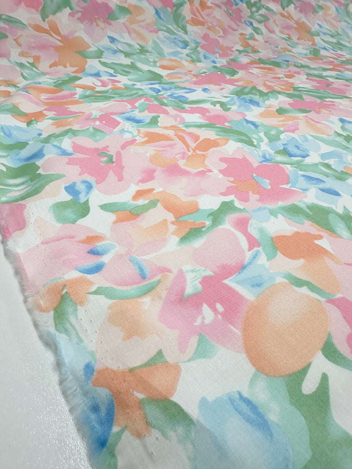 A detailed view of the Printed Cotton - Blossoms - 150cm by Super Cheap Fabrics displays an array of pastel hues, including pink, peach, green, and blue. Crafted from natural cotton fibers, this fabric showcases an abstract design of painterly flowers and leaves, resulting in a soft and vibrant visual appeal suitable for various applications.