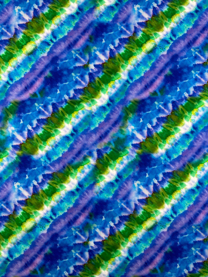 The Printed Cotton - Lizard - 150cm by Super Cheap Fabrics features a vibrant and dynamic abstract pattern with diagonal stripes in shades of blue, green, and purple. This design resembles a watercolor tie-dye effect on lightweight printed cotton fabric, highlighting its textured appearance made from natural cotton fibers.