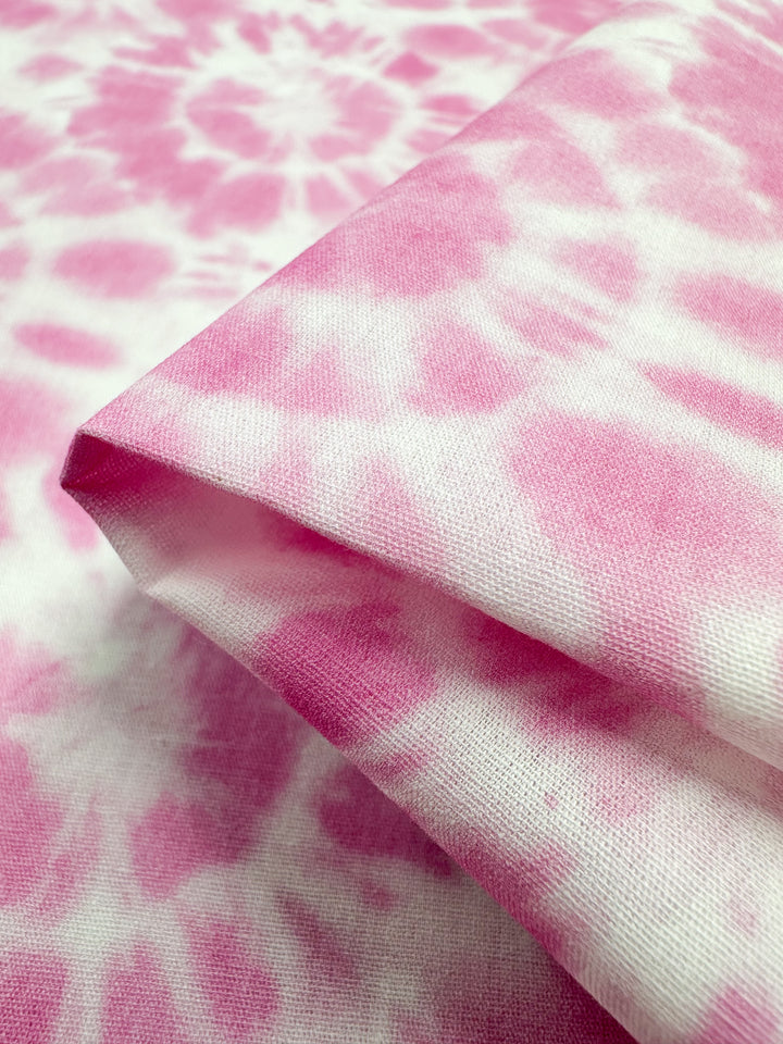 A close-up view of the Printed Cotton - Rosebloom - 150cm from Super Cheap Fabrics, highlighting its geometric patterns in pink and white tie-dye on a cotton base. The folded fabric displays its rich texture and color variations.