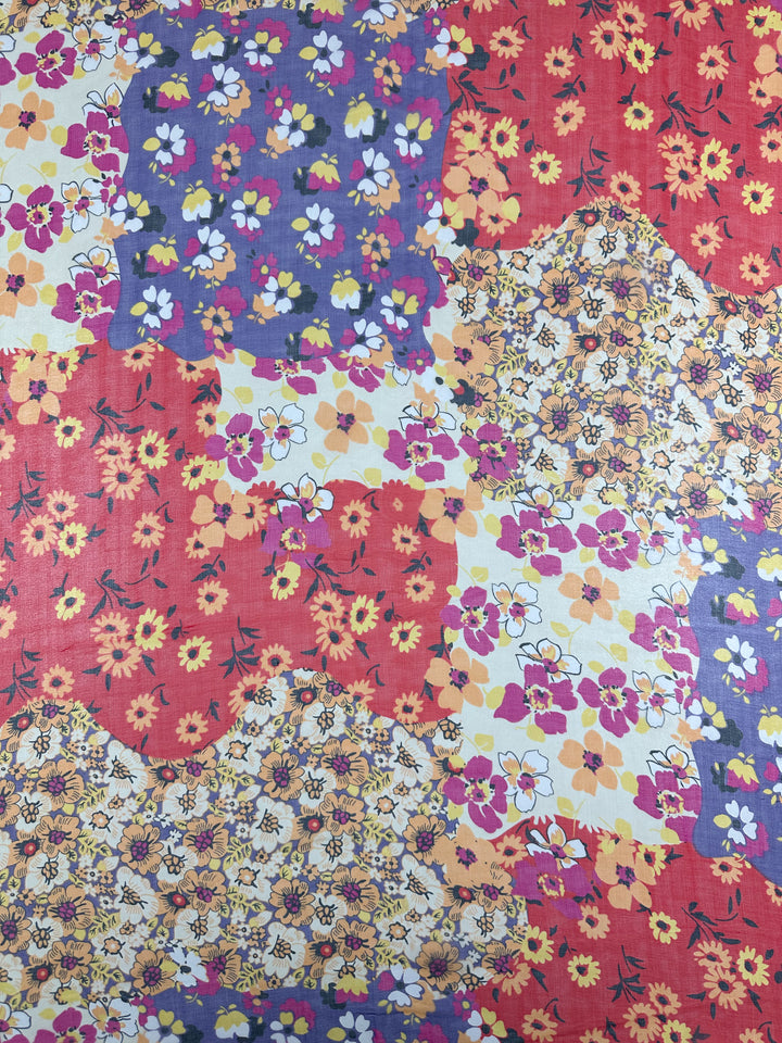 The Florazard Printed Silk from Super Cheap Fabrics features a vibrant quilt pattern crafted from extra lightweight silk, incorporating patches of red, blue, yellow, and white. Each section showcases small flowers in various hues, creating a lively and colorful design that mirrors the elegance of delicate silk dresses. The fabric is 140cm wide.