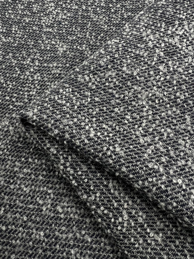 Close-up of a folded piece of Wool Boucle Blend - Repeater - 150cm by Super Cheap Fabrics. The texture shows a mix of intertwined threads, creating a speckled appearance with light and dark tones. Perfect for overcoats, the fabric looks tightly woven and dense. Expertly crafted in Italy.
