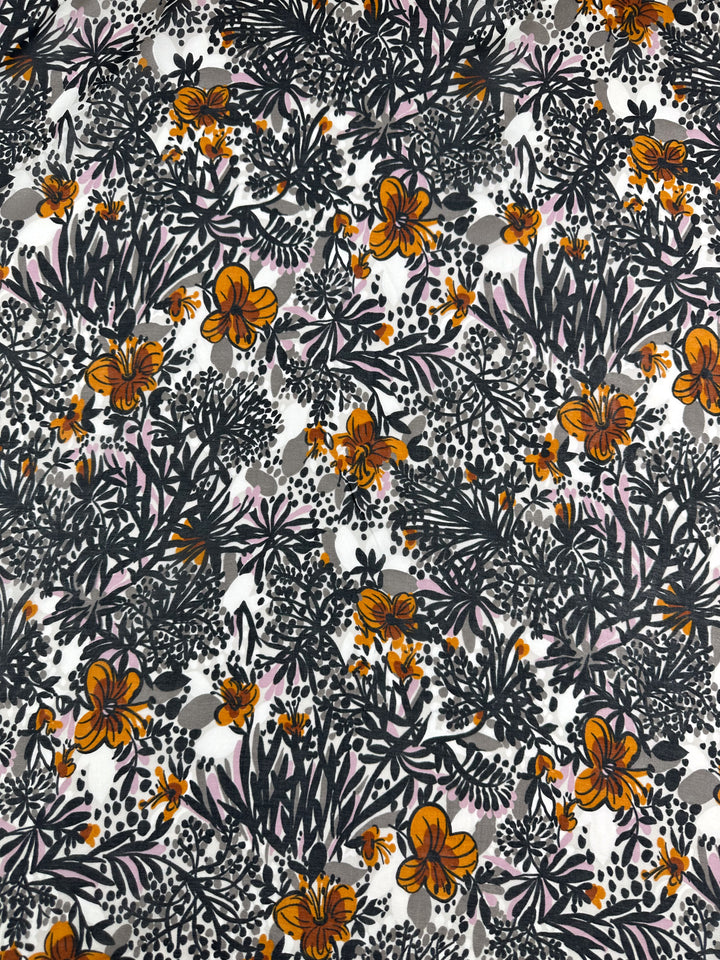 The Printed Silk Voile - Garzen, offered by Super Cheap Fabrics, showcases a lively floral pattern with orange flowers, black leaves, and assorted plants against a white background. This intricate design delivers a vibrant and dynamic look, making it ideal for extra lightweight clothing accessories. The fabric width is 140cm.