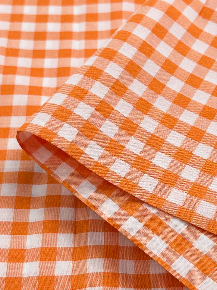 Super Cheap Fabrics' Cotton Gingham in Mid Orange, spanning 112 cm, features a neatly folded orange and white checkered pattern crafted from natural cotton fibers.