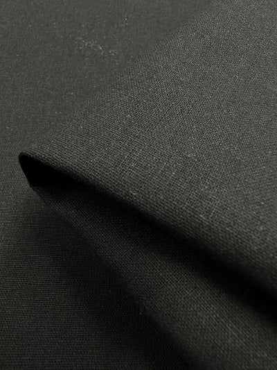 A close-up view of the smooth, deep black Ramie Linen by Super Cheap Fabrics, measuring 150cm in width, folded over itself to showcase the texture and weave of its natural fibers.