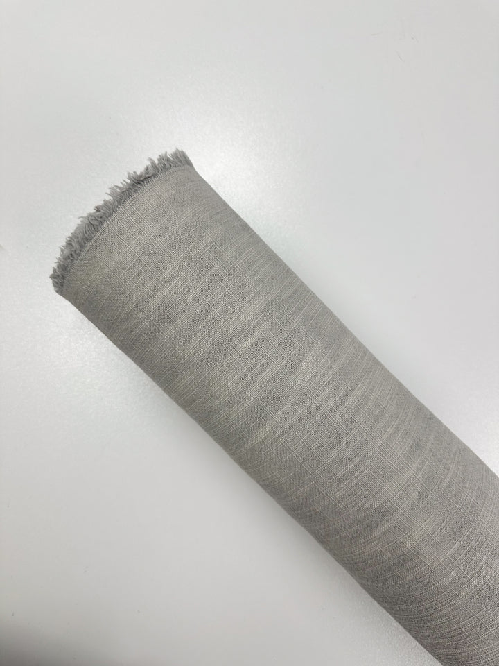 A roll of Basket Dyed Cotton - Dove by Super Cheap Fabrics lies on a white surface. The fabric features a subtle grid pattern, and its slightly frayed edge marks the beginning of the roll. The heavy weight of the 140cm wide cotton suggests it is durable for long-lasting use.