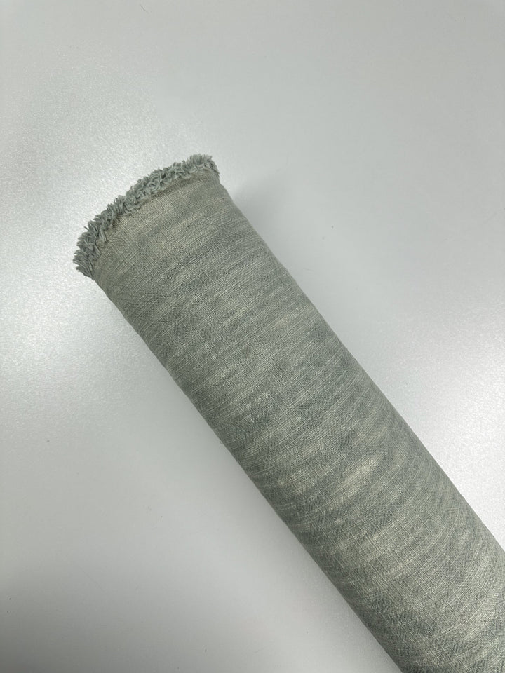 A close-up of the Basket Dyed Cotton - Sea Mist - 140cm fabric roll, showcasing its textured heavyweight cotton surface and frayed edge, set against a smooth white backdrop. The fabric is from Super Cheap Fabrics.