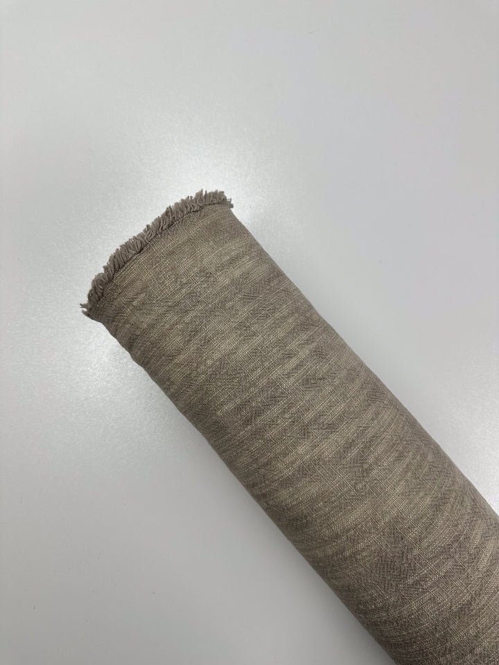 A roll of taupe Basket Dyed Cotton by Super Cheap Fabrics, measuring 140cm wide, is displayed against a plain white background. Showcasing a twill weave and a frayed edge at the top, this durable upholstery fabric combines resilience with style.