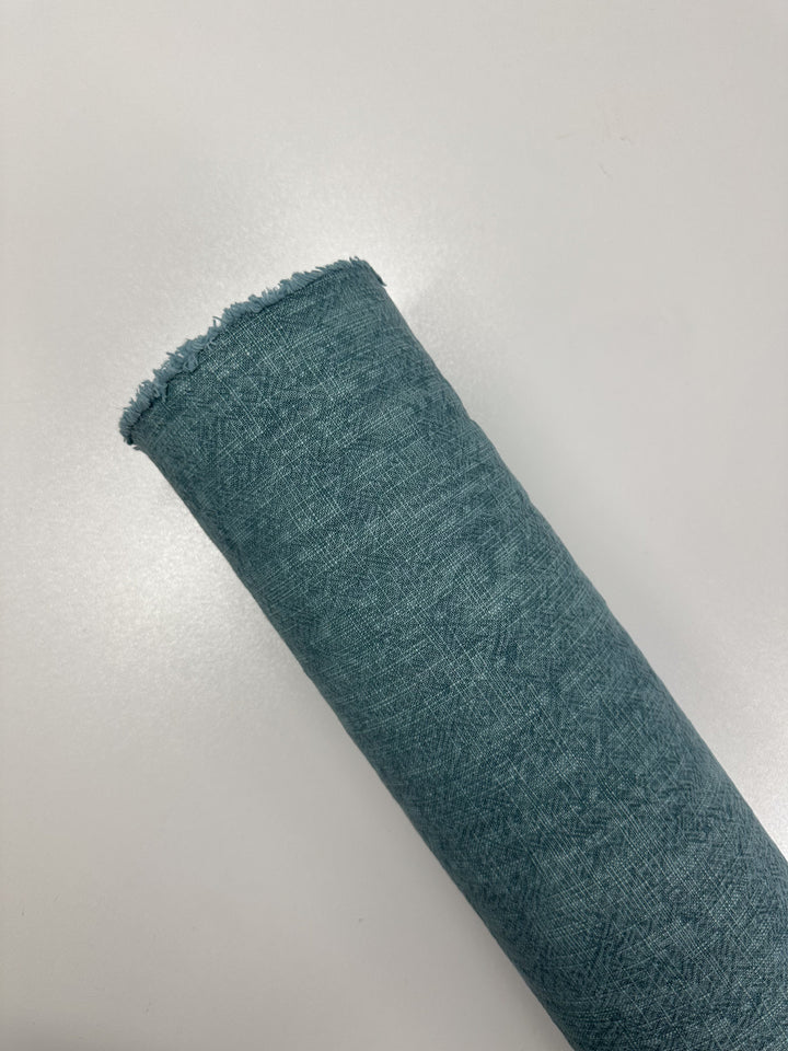 A rolled-up piece of the Basket Dyed Cotton - Peacock - 140cm by Super Cheap Fabrics, featuring a blue textured surface and a frayed edge, is placed on a plain white background.