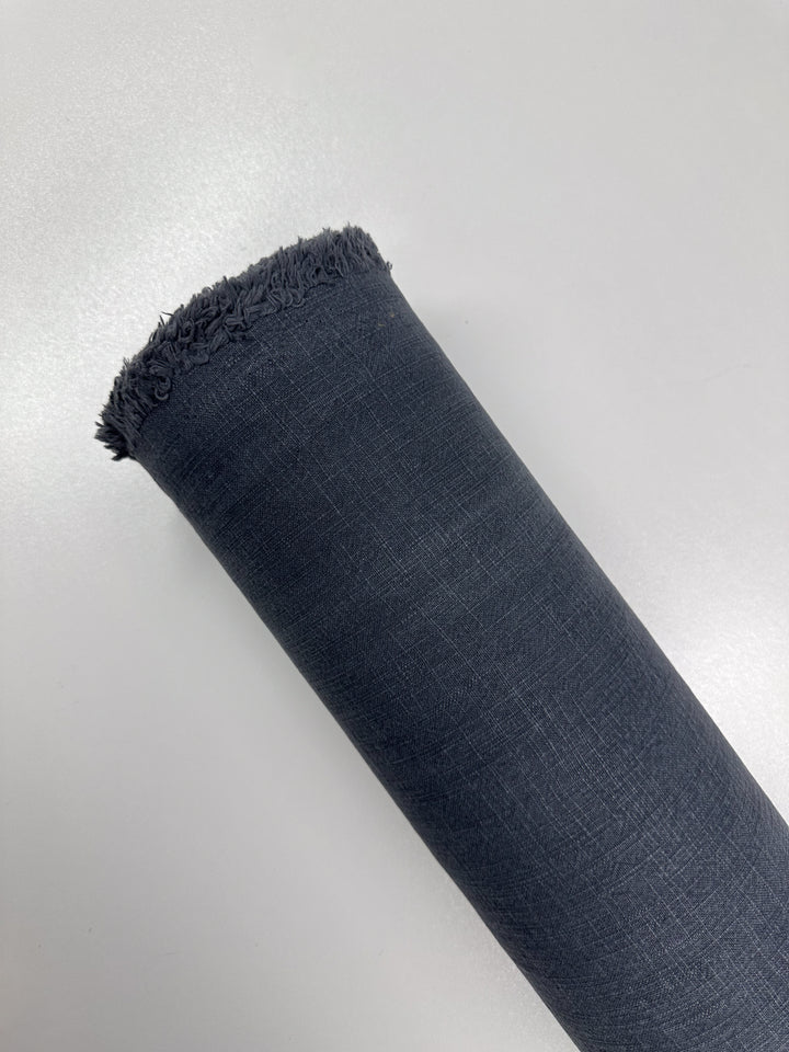 A rolled-up piece of navy Basket Dyed Cotton from Super Cheap Fabrics, featuring a fringe on one end, is displayed on a white surface to highlight its twill weave.