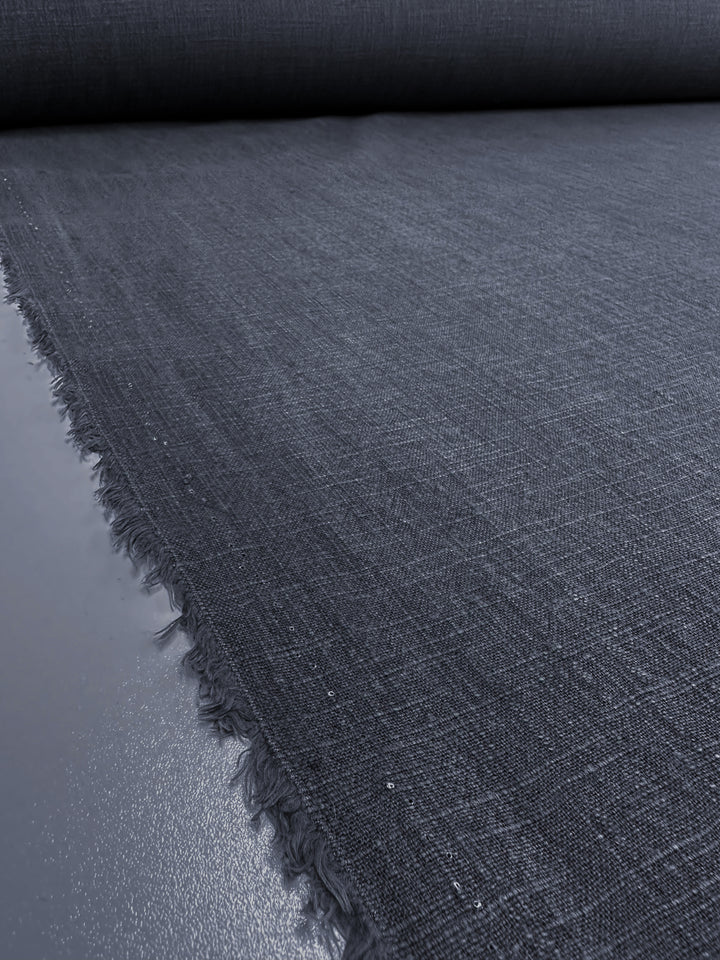 A close-up of a dark navy fabric roll from Super Cheap Fabrics' Basket Dyed Cotton collection rests on a flat surface. The substantial material displays a subtly textured pattern with frayed edges, indicating its twill weave construction.