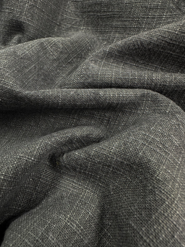 A close-up view of Basket Dyed Cotton in Charcoal, from Super Cheap Fabrics, reveals its dark gray woven upholstery with a textured and slightly crumpled surface, showcasing interlaced threads and a subtle sheen.