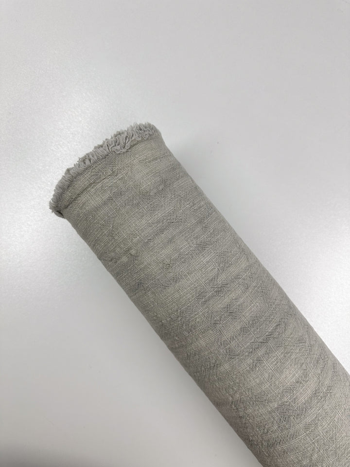 The fabric shown is "Basket Dyed Cotton - Moonstruck - 140cm" by Super Cheap Fabrics, featuring a roll of light gray, 100% cotton material with frayed edges and a subtle twill weave set against a plain white background.