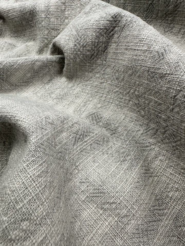 A close-up of the Basket Dyed Cotton - Moonstruck - 140cm by Super Cheap Fabrics reveals its textured gray upholstery fabric with subtle crisscross patterns, enhanced by soft folds and creases that highlight its intricate twill weave.