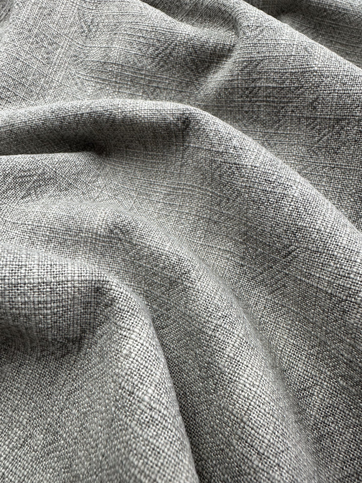 Close-up of Super Cheap Fabrics' Basket Dyed Cotton in silver grey, featuring a textured twill weave pattern. The 140cm wide upholstery fabric is slightly draped, creating soft folds and shadows.