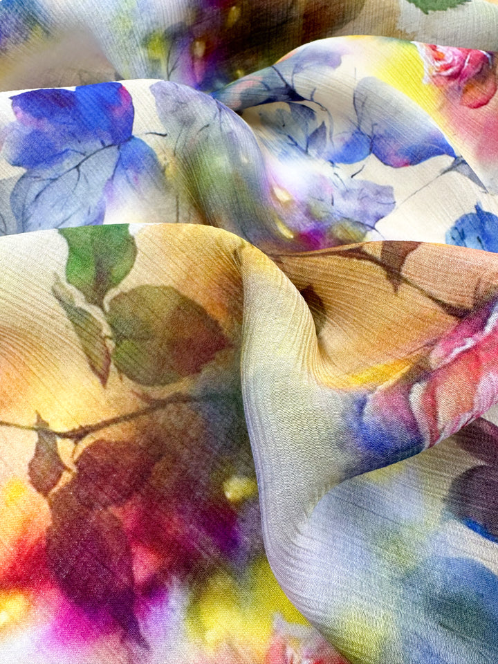 A close-up photo of the "Designer Cotton - Isabelle - 150cm" by Super Cheap Fabrics showcases a luxurious sewing project. It features swirling patterns in vibrant blues, purples, pinks, and greens that blend seamlessly to create an impressionistic floral effect.