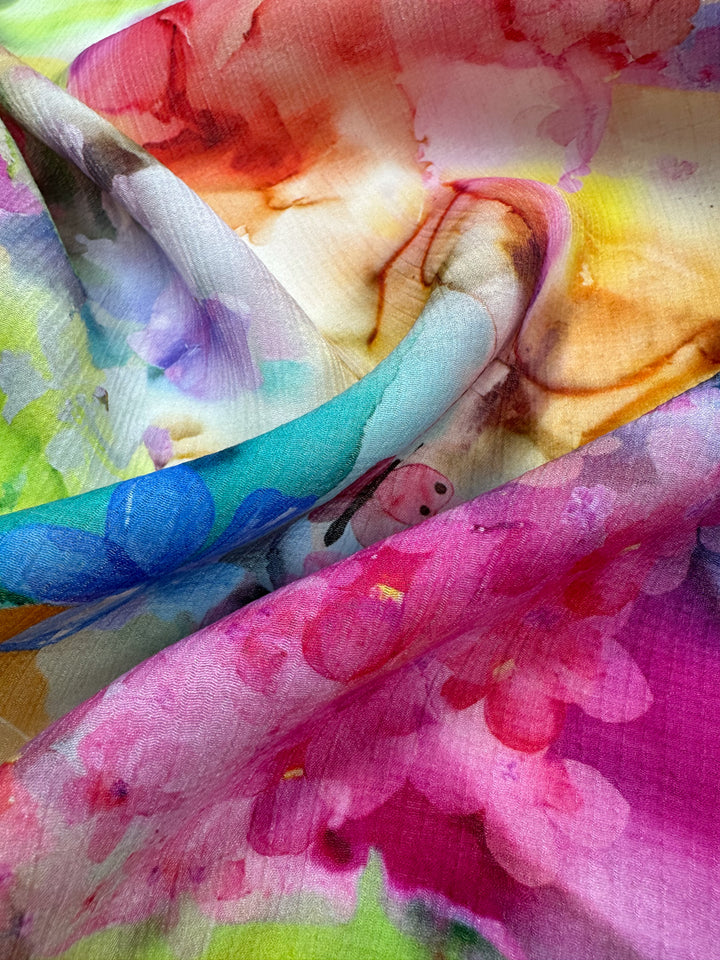 A close-up of "Designer Cotton - Alice - 150cm" by Super Cheap Fabrics, featuring a vibrant multicolored design with abstract floral patterns. The fabric highlights shades of pink, blue, green, and yellow, offering a flowing and textured appearance ideal for luxury sewing projects.