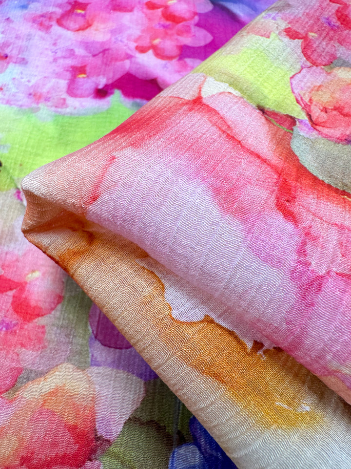 A close-up view of the vibrant Designer Cotton - Alice - 150cm from Super Cheap Fabrics, featuring a lightweight cotton fabric with a watercolor floral pattern in bright pink, orange, yellow, and green hues. The fabric is layered and folded to highlight its vivid design—ideal for luxury sewing projects.