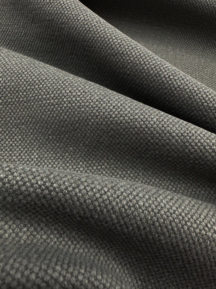 A close-up of the Canvas Linen Denim in Brushed Nickel from Super Cheap Fabrics reveals its dark gray, textured woven pattern. The material softly gathers into gentle folds, adding depth and softness, making it an ideal choice for enhancing home décor.