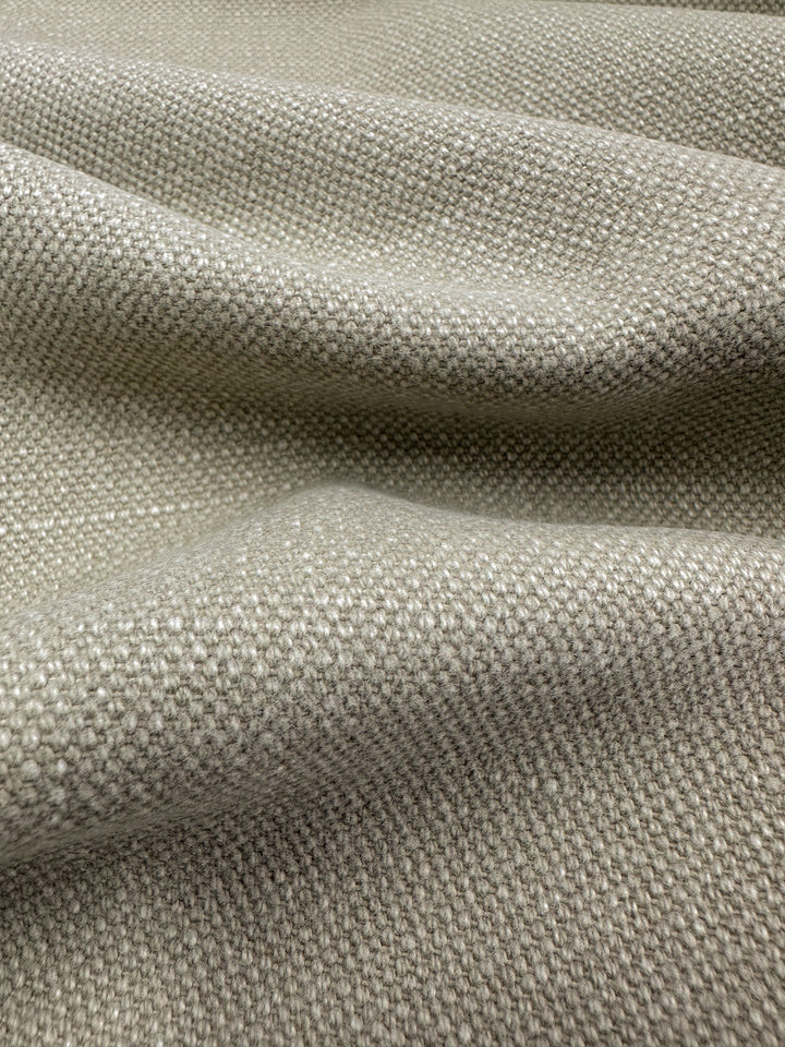 A close-up view of the Canvas Linen Denim - Peyote fabric from Super Cheap Fabrics, showcasing its textured beige upholstery with a woven pattern, gentle folds, and soft lighting that highlights its intricate details.