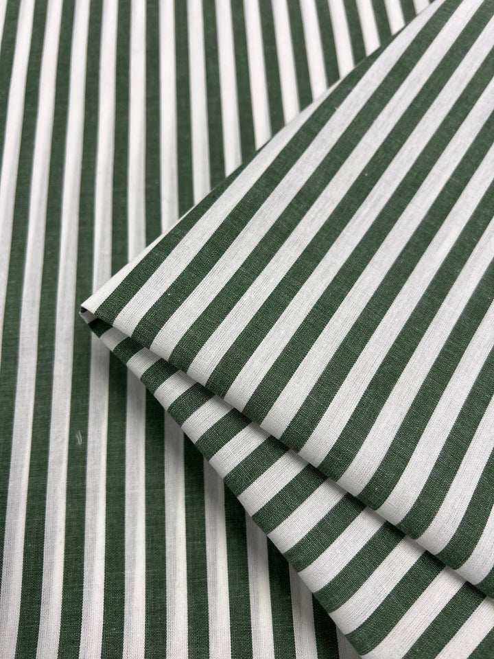 Close-up of folded Super Cheap Fabrics' Cotton Lawn - Fir, showcasing a pattern of evenly spaced thick green and white vertical stripes. The neatly pressed 100% cotton fabric, measuring 150cm wide, displays sharp creases at the folds for a consistent and orderly design.