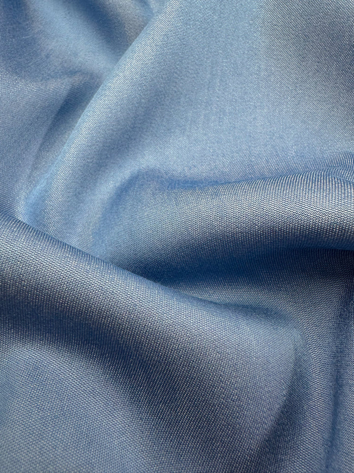 A close-up of the Chambray fabric by Super Cheap Fabrics, elegantly draped in gentle waves and highlighting the serene hue of Blissful Blue, offers a glimpse of its soft, lightweight texture.